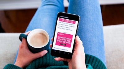 Un cliente con un teléfono que muestra un anuncio personalizado de T-Mobile en una mano y un café en la otra.